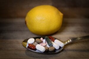 Silver spoon holding a variety of colorful supplement tablets and capsules with a whole lemon in the background.