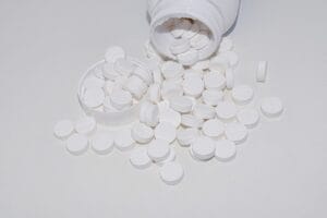 Numerous magnesium tablets spilling out of an open bottle and cap onto a clean white surface