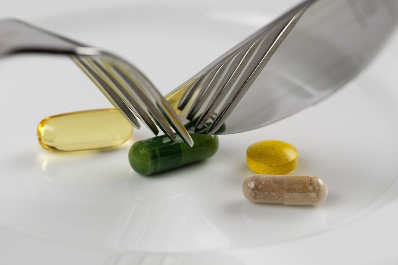 Assorted nutritional supplement capsules and tablets on a white plate with a fork and knife