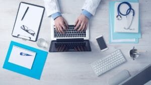 Overhead view of a doctor's desk with a laptop, stethoscope, medical charts, and office supplies