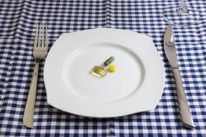 A small assortment of health supplement capsules and tablets centered on a white plate with a fork and knife on a blue checkered tablecloth