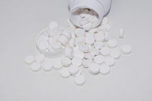 Numerous magnesium tablets spilling out of an open bottle and cap onto a clean white surface