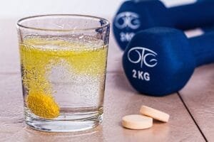 Yellow effervescent vitamin tablet dissolving in a glass of water next to 2kg blue dumbbells