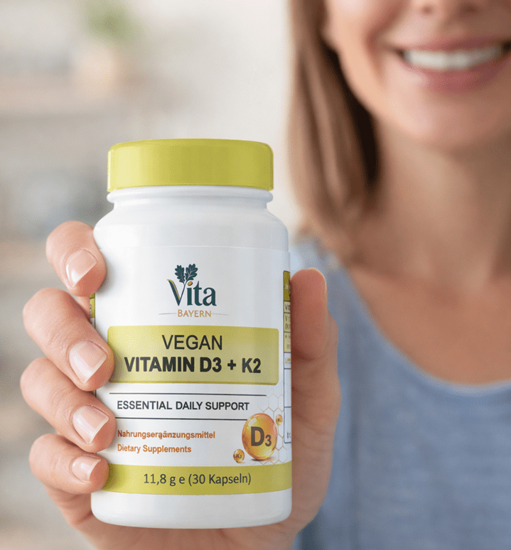 A close-up of a person holding a bottle of Vita Elixia Vegan Vitamin D3 + K2 "Essential Daily Support" dietary supplement capsules