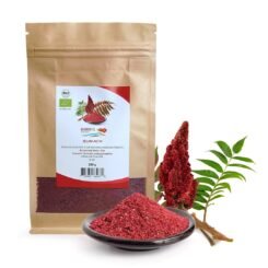 A 200g brown paper pouch of Blumental Organic Sumac next to a small bowl of deep-red spice powder and a fresh staghorn sumac branch.