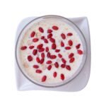 A top-down view of a white bowl containing creamy yogurt topped with a generous serving of bright red, dried organic barberries.