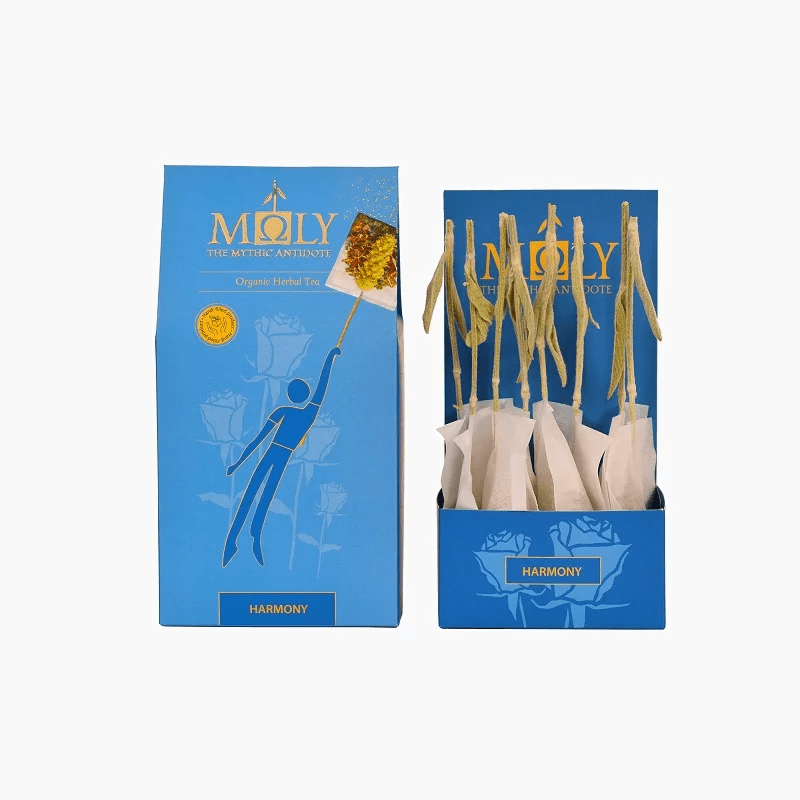 Blue retail box for Moly "Harmony" Organic Herbal Tea shown next to an open display box containing individually wrapped tea bags with natural herbal stem stirrers.