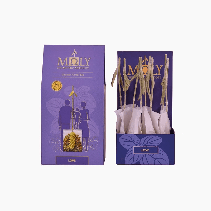 Purple retail box for Moly "Love" Organic Herbal Tea shown next to an open display box containing individually wrapped tea bags with natural herbal stem stirrers.